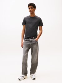 Gray textured t-shirt, loose-fit light gray jeans, and white sneakers with black accents. Model stands with hands in pockets against plain background.