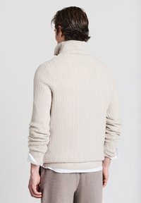 Maglione beige lavorato a maglia con collo alto e texture a coste, caratterizzato da maniche lunghe e una vestibilità leggermente larga. Dettagli sottili in tutto il capo.