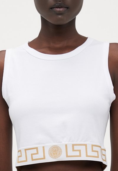 Bílý bezrukávový crop top vyrobený z hladkého bavlněného materiálu, s námořnickým zlatým vzorem řeckého klíče a emblémem Medúzy na lemu.
