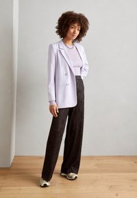 Dobbeltspent lilla blazer over en lys lilla topp, kombinert med høyt midje, svarte, teksturerte vide bukser og stilige sneakers med gullakcenter.