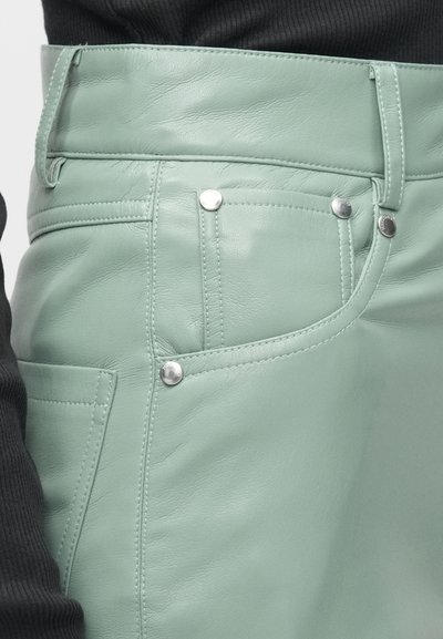 Mėtų žalios odos sijonas su sidabro detalėmis, su priekinėmis kišenėmis ir siūlėmis, pateiktas šalia juodo rausvo džemperio.