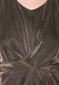 Metallisk taupe-klänning med v-ringning, draperat tyg och en definierad midja med veck, som visar en slät, reflekterande yta.