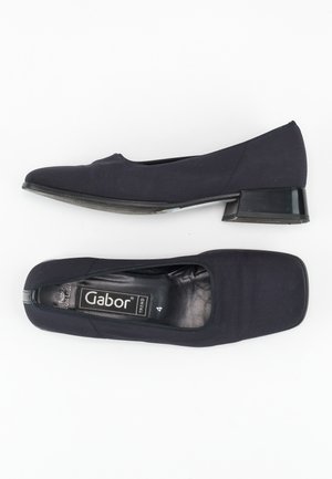 Černé baletní ploché boty z látky se čtveratou špičkou a nízkým, obdélníkovým průhledným podpatkem. Měkký svrchní materiál s minimálním šitím a logem uvnitř.