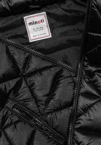 Schwarze gesteppte Jacke mit glänzender Außenfläche, ausgestattet mit einer Tasche mit Reißverschluss und einem Etikett, das die Größe 8-9 Jahre angibt. Hergestellt in Myanmar.