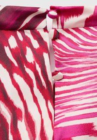 Tela estampada con espirales abstractas en rojo y rosa, con rayas blancas contrastantes. Incluye botones para el cierre en un borde doblado.