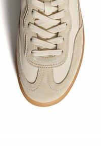 Zapatilla beige con cordones que presenta un upper de cuero suave, acentos de ante, detalles cosidos y una suela de goma.