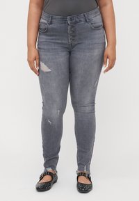 Gray skinny jeans featuring a high buttoned waist, distressed accents, and a fitted design, paired with black flat shoes with studs.