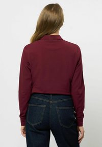 Languesleeve bordeaux polo shirt met een eenvoudige kraag, gecombineerd met donkere spijkerbroek met twee achterzakken en gele stikselaccenten.