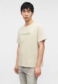 Μπεζ βαμβακερό T-shirt με κοντά μανίκια και στρογγυλή λαιμόκοψη. Διακοσμημένο με ανάγλυφο λογότυπο «MICHAEL KORS» στο στήθος. Απλός σχεδιασμός και άνετη εφαρμογή.