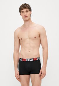 Čierne boxerky s kontrastným bielym a červeným pásom s nápisom "DIESEL". Vyrobené z hladkej látky, so priliehavým strihom a krátkou dĺžkou.