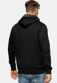 Sort hættebluse i en blød tekstur, med en trykt krave og ribbede manchetter og kant. Bæres med lyseblå denimjeans.