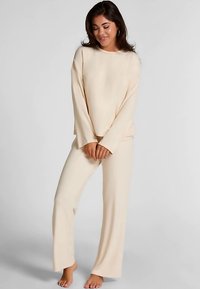 Beige loungewear-set gemaakt van zachte stof, bestaande uit een top met lange mouwen en losse broek. Simpel ontwerp met een ontspannen silhouet.