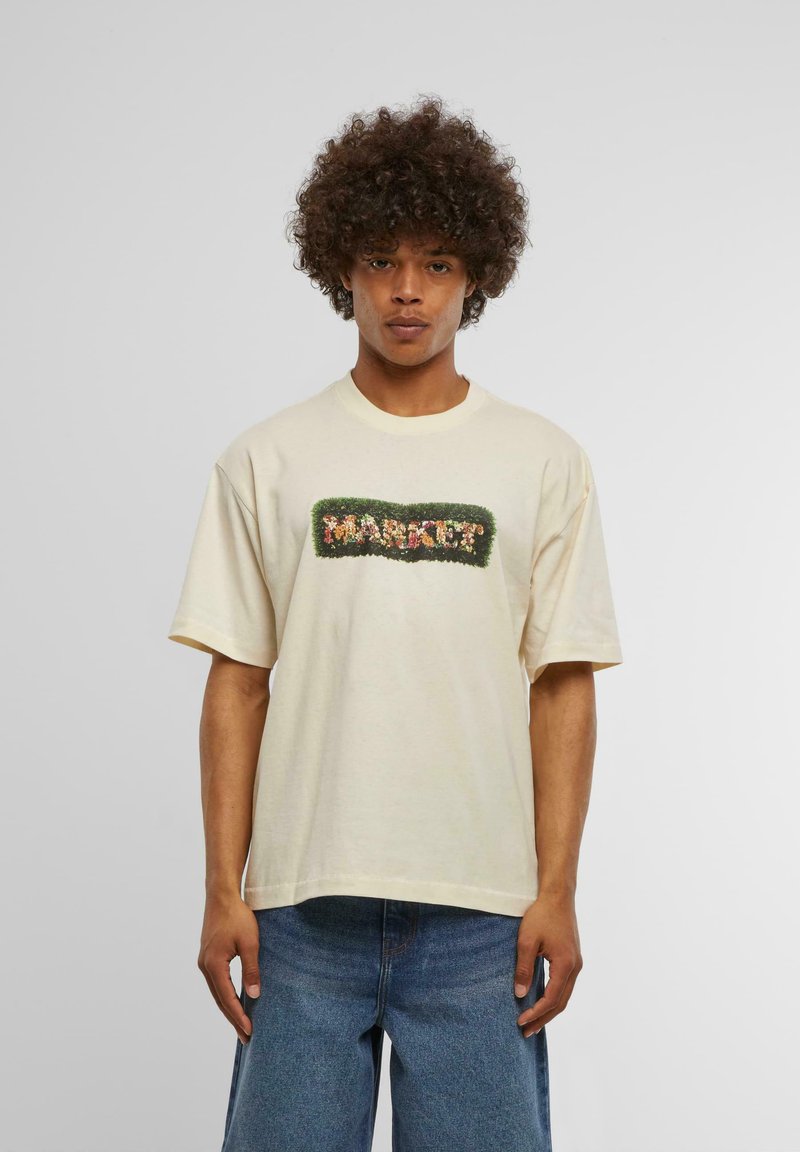 Lys beige bomulls t-skjorte med løs passform, som har et grønt brodert "MARKET?" design omkranset av fargerike blomsterdetaljer.