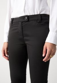 Černé slim-fit kalhoty s hladkou texturou, zapínání na knoflík a přední kapsy, v kombinaci s bílou košilí na knoflíky.