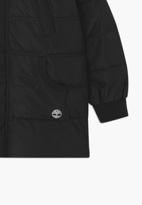 Giubbotto nero invernale con texture cucita, tasca con zip, polsini a maglia e un piccolo logo argento sulla tasca anteriore.