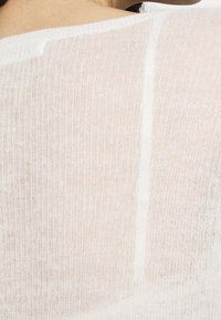 Weißes, leichtes Strickoberteil mit strukturierter Oberfläche und feiner Rippstruktur. Verfügt über einen weiten Ausschnitt und eine lockere Passform.