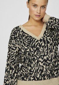 Sweter z dekoltem w serek w czarno-beżowy wzór zebry. Ma długie rękawy i prążkowane wykończenia. Wykonany z dzianiny.