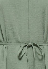 Groen jurkje gemaakt van gestructureerde stof met een strikceintuur in de taille. Heeft een ontspannen pasvorm en een zachte, vloeiende uitstraling.