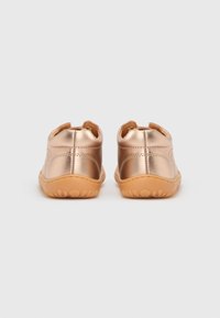 Ζεύγος μεταλλικών ροζ χρυσών παπουτσιών για νήπια με καφέ λαστιχένιες σόλες, ορατά από πίσω σε απλό λευκό φόντο.