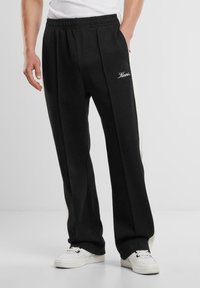 Sorte sweatpants med hvide sidelæg, elastisk talje og frontfold. Har broderet logo på hoften og en slank, tætsiddende pasform.