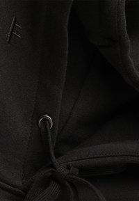 Black hoodie interior featuring soft fabric, adjustable drawstring with metal eyelet, and discreet embroidered logo on fabric.