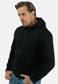 Czarna bluza z kapturem z regulowanymi sznurkami, przednia kieszeń i ściągacze przy mankietach. Połącz z jasnoniebieskimi dżinsami. Miękki materiał i swobodny krój.