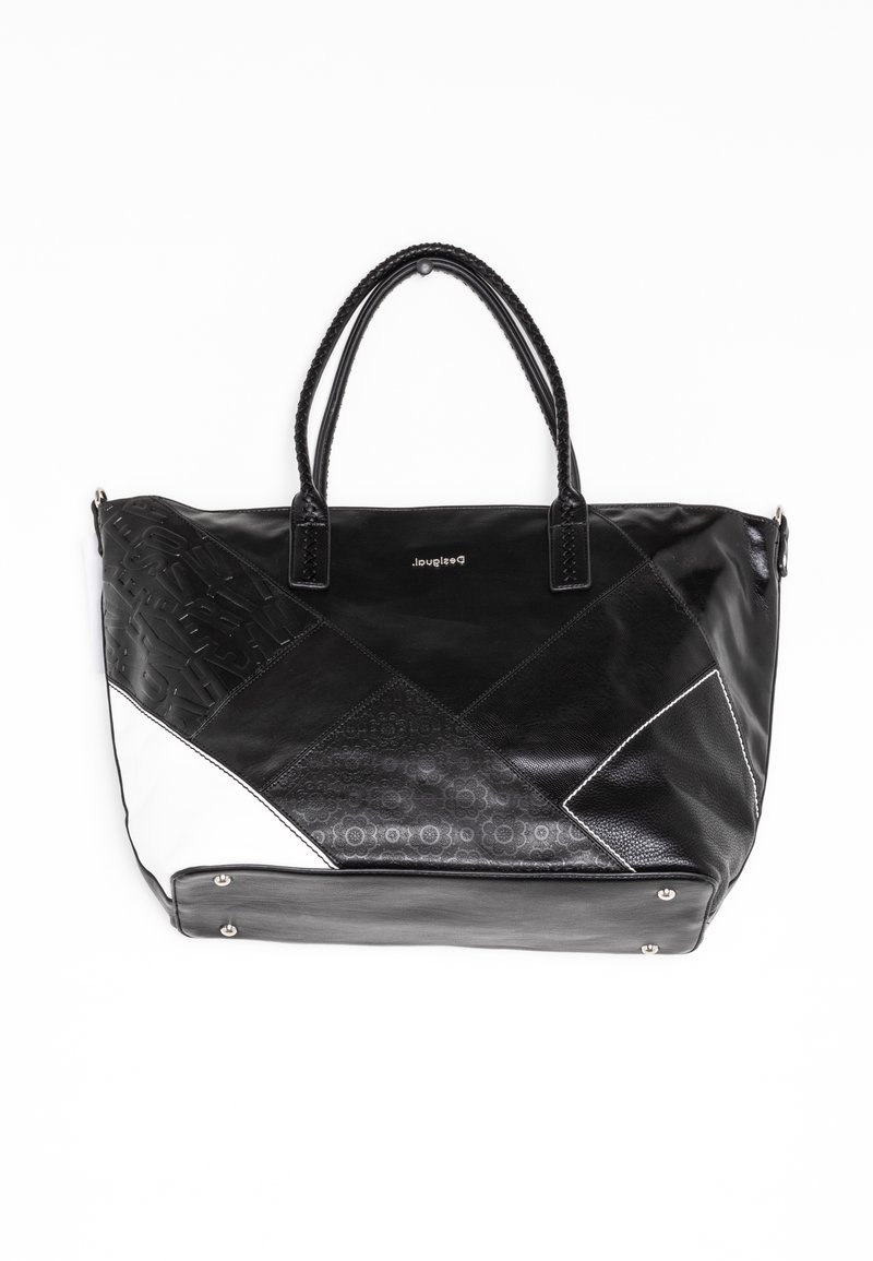 Grand sac cabas en cuir noir et blanc avec anses tressées, motif patchwork et petits clous métalliques aux coins inférieurs.