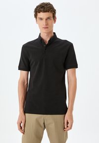 Svart polo skjorta med krage, korta ärmar, placket med tre knappar och en åtsittande design. Slät tyg med minimala sömdetaljer.