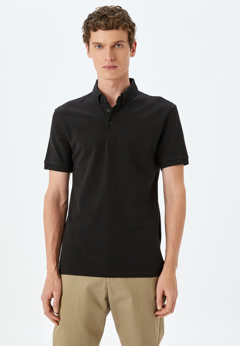 Svart polo skjorta med krage, korta ärmar, placket med tre knappar och en åtsittande design. Slät tyg med minimala sömdetaljer.