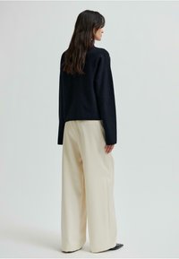 Czarny sweter z długim rękawem zestawiony z kremowymi spodniami szerokimi w nogawkach. Sweter ma luźny krój, a spodnie wykonane są z gładkiego, teksturowanego materiału.