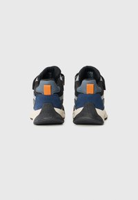 Scarpe sportive con una combinazione di nero, blu navy, grigio e dettagli arancioni. Suola in gomma testurizzata con collo imbottito e cinturini regolabili.