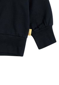 Schwarzer Sweatshirtbund aus weichem Baumwollstoff. Verfügt über einen gerafften Ärmelsaum und ein kleines gelbes Etikett mit Logodetail. Strukturierten Rippbündchen.