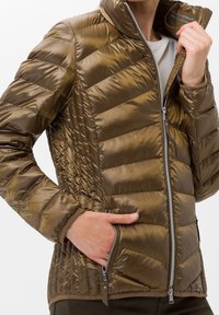 Brun pufferjacka med en glänsande, quiltad textur, hög krage, fickor med dragkedja och figursydd design med kontrasterande bruna detaljer.
