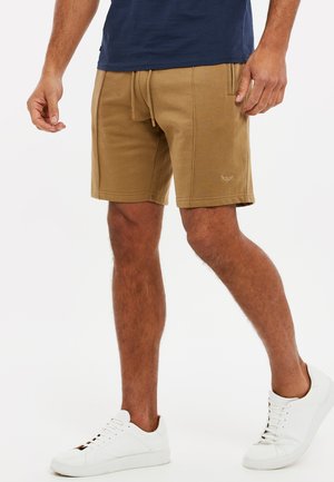 Beige Baumwollmischung-Shorts mit elastischem Taillenbund und Kordelzug, ausgestattet mit seitlichen Taschen und dezentem Logo-Detail. Kombiniert mit weißen Sneakern.