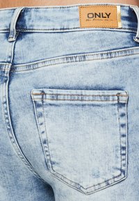 Lyseblå denimjeans med et merke merket "ONLY." Har en baklomme, synlig søm og en falmet tekstur.