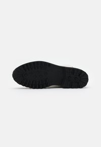 Sole di scarpa in gomma nera con profonde scanalature per la trazione e un design circolare. Bordo liscio con nervature rialzate per una maggiore presa.