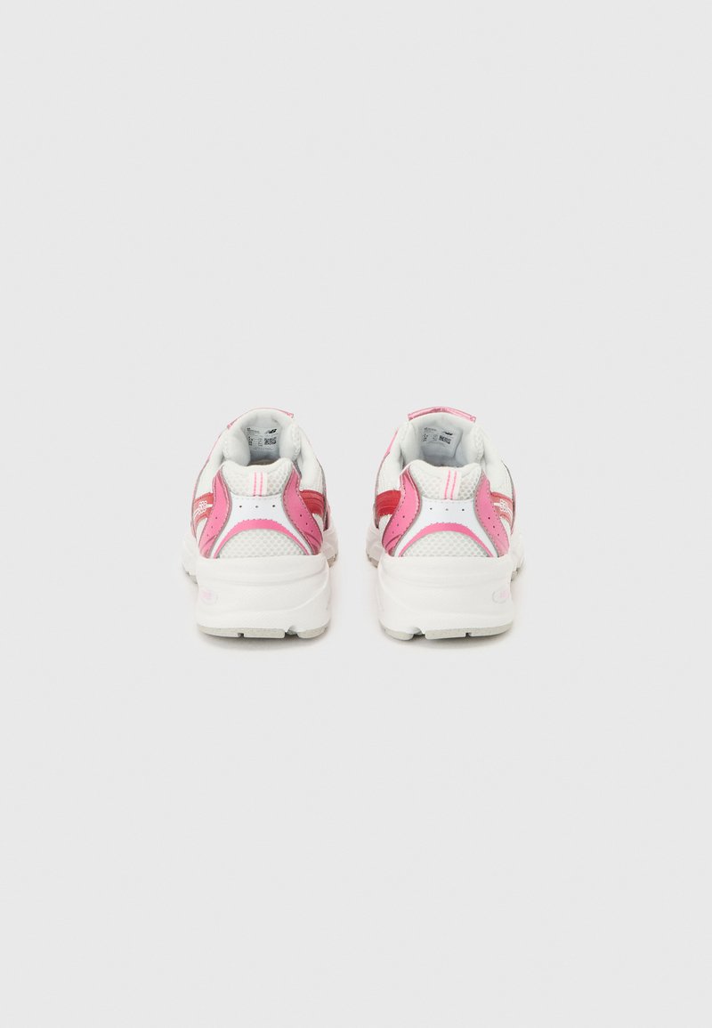 Paire de chaussures de sport blanches avec des accents roses et rouges, vues de dos sur un fond gris clair uni.