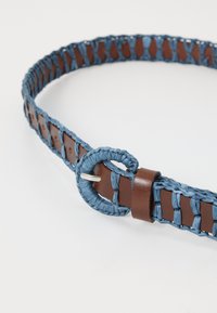 Woven öv, kék fonott anyaggal, barna bőr kiegészítőkkel, kör alakú csattal és tartós, texturált felülettel.