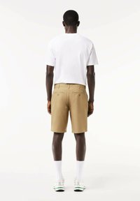 Pantaloni corti color khaki con un taglio dritto, due tasche posteriori e una piccola toppa con logo. Abbinati a una t-shirt bianca a maniche corte semplice.