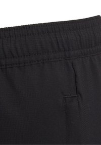 Zbliżenie na czarne materiałowe spodnie, pokazujące elastyczny pas oraz szczegóły przeszyć bocznych kieszeni.