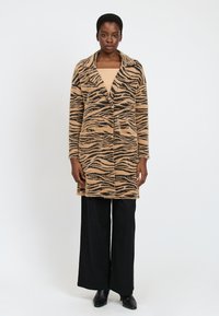Tans- og sorte stribede, mellemlange, fluffy cardigan med sjalskrave, sidelommer, båret over en beige top og sorte vidde bukser.