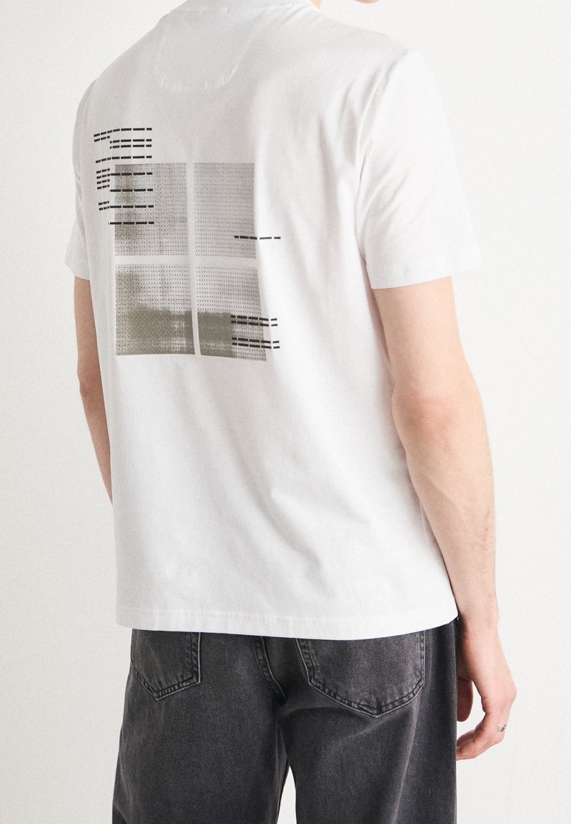 T-shirt en coton blanc à manches courtes, avec un motif imprimé au dos en noir et vert olive, et un ourlet droit.