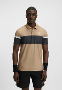 Beige og marineblå stribet polo shirt med et rutenet mønster, korte ærmer, krave og logo. Båret med sorte shorts og et sort håndledsbånd.