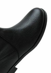 Bottine en cuir noir, présentant une surface texturée, un bout arrondi, des coutures discrètes et une semelle en caoutchouc plate.