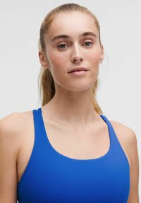 Blå atletisk linne med rundad halsringning och smala axelband, tillverkat av slät tyg. Minimalistisk design, inga synliga mönster.