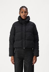 Black cropped puffer jacket with a textured surface, high collar, front zipper, and long sleeves, paired with dark fabric trousers.