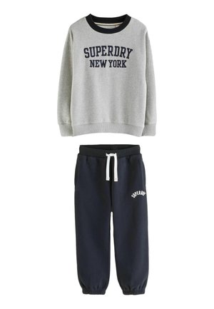 Šedá mikina s nápisem "SUPERDRY NEW YORK" v kombinaci s námořnickými jogger kalhotami s bílým šňůrkovým stahováním a logem "SUPERDRY" na stehně.