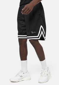 Shorts de sport noirs avec des rayures blanches sur les côtés et un détail signature. Fabriqués en tissu léger, ils présentent une coupe ample et une taille élastique.