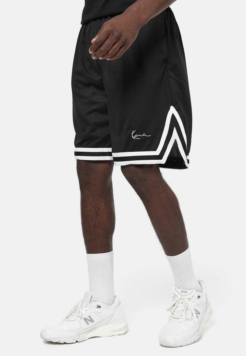 Shorts de sport noirs avec des rayures blanches sur les côtés et un détail signature. Fabriqués en tissu léger, ils présentent une coupe ample et une taille élastique.