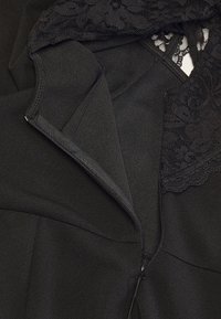 Schwarzes Kleid aus Stoff mit einer Spitzenoverlay am Ausschnitt. Das Kleid verfügt über einen Reißverschluss und eine glatte, matte Textur.